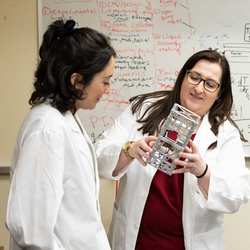 Professor in lab coat conducting research with student